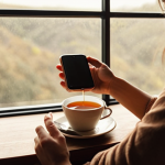 A person enjoying a cup of tea while looking out the window, smartphone set aside, conveying a sense of peace and disconnection from technology. Warm, muted colors, soft lighting.